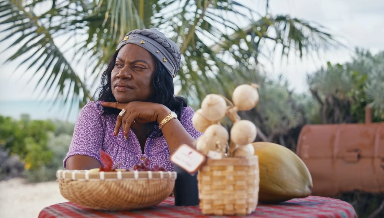 A seated Turks and Caicos cultural bearer with handmade woven baskets beneath palm trees