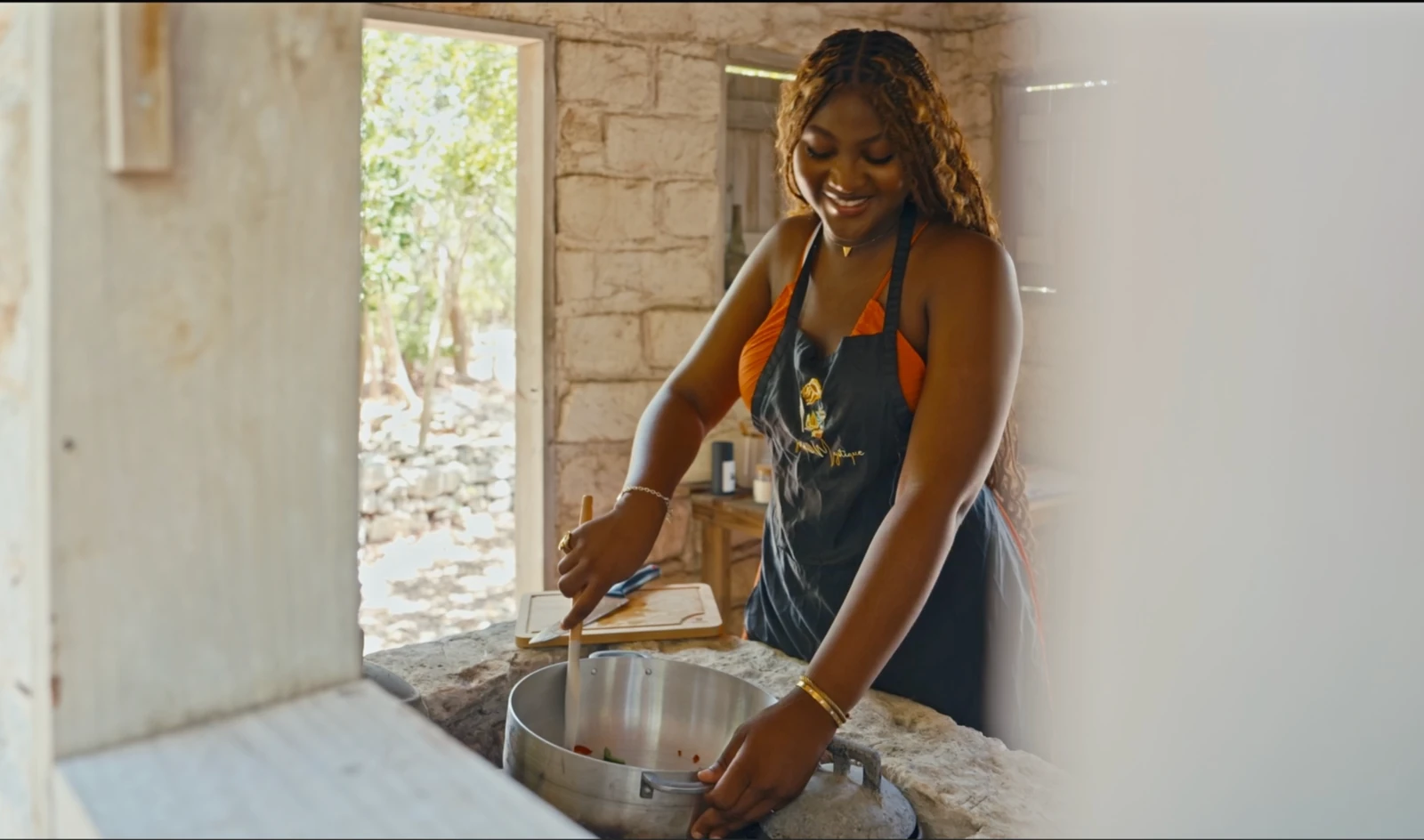 An Island Mystique host preparing island food in a stone kitchen, wearing a fabric apron