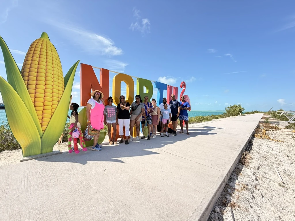 Island Mystique guests beside the colourful North Caicos welcome sign under a blue sky